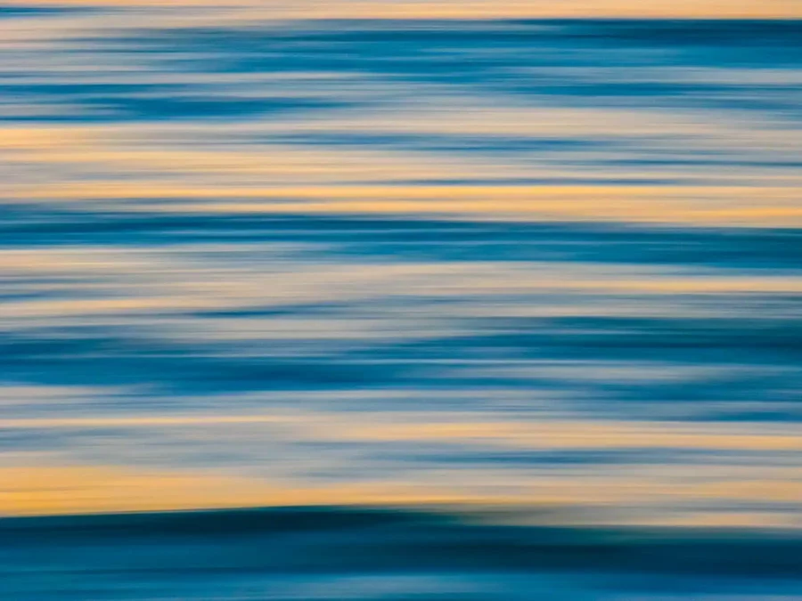תמונה מופשטת מטושטשת של גלי ים בתנועה, משלבת גווני כחול וזהב כדי ליצור נוף של ים ושלווה