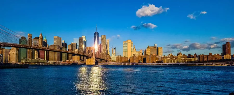 זריחה מעל קו הרקיע של העיר ניו יורק עם גשר ברוקלין וקרני השמש משתקפים כשביל על המים