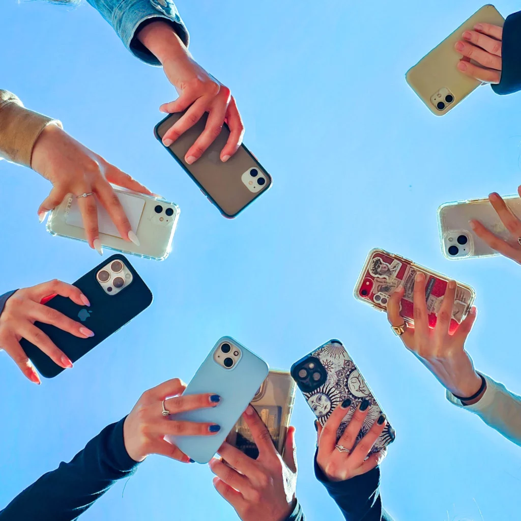 חבורת חברים מחזיקה סמארטפונים מול שמיים כחולים בהירים, ממחישה את החיבור המודרני דרך הטכנולוגיה