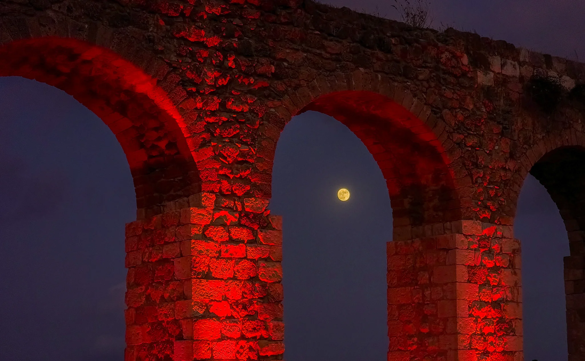 הירח המלא ממוקם בצורה מושלמת בין קשתות אמת המים העתיקה בקיבוץ לוחמי הגטאות בישראל, מתחת שמים אפלים.