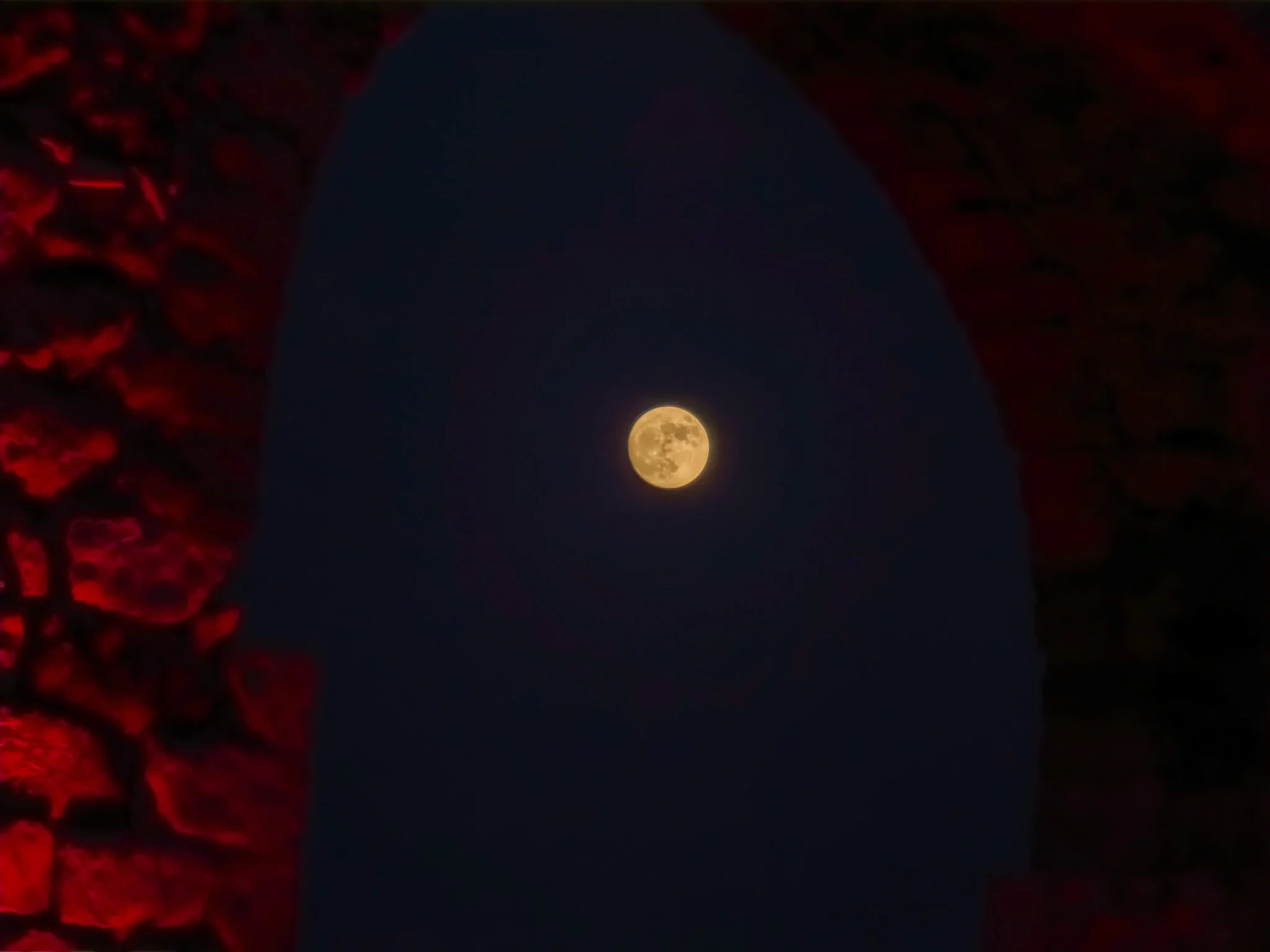 הירח מופיע במרכזו בשמי הלילה דרך קשת גשר של אמת מים עתיקה בקיבוץ לוחמי הגטאות, כאשר אבני הקשת זוהרות באדום.