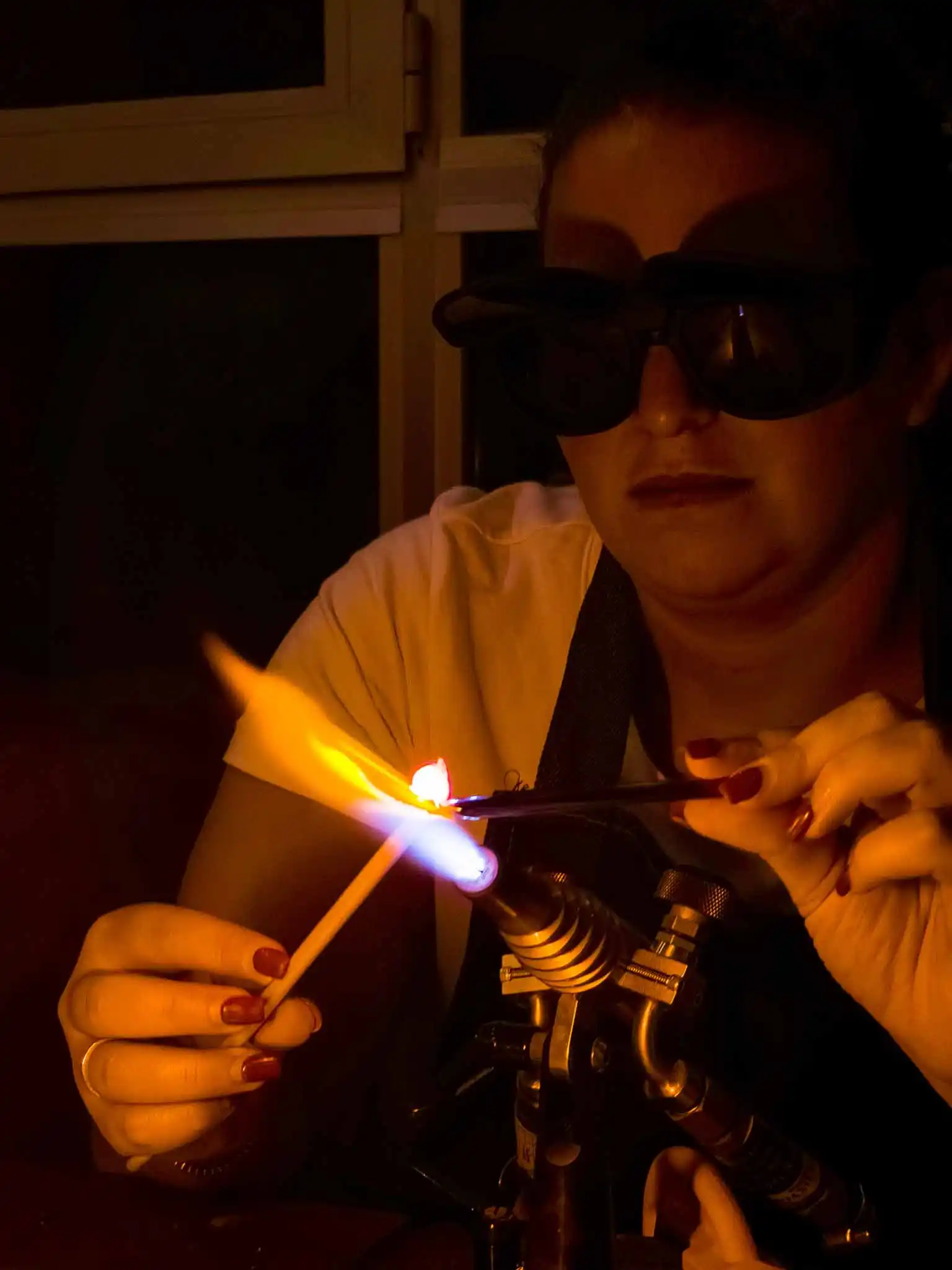 אישה עובדת עם זכוכית חמה באמצעות להבת אש בסדנת פיסול