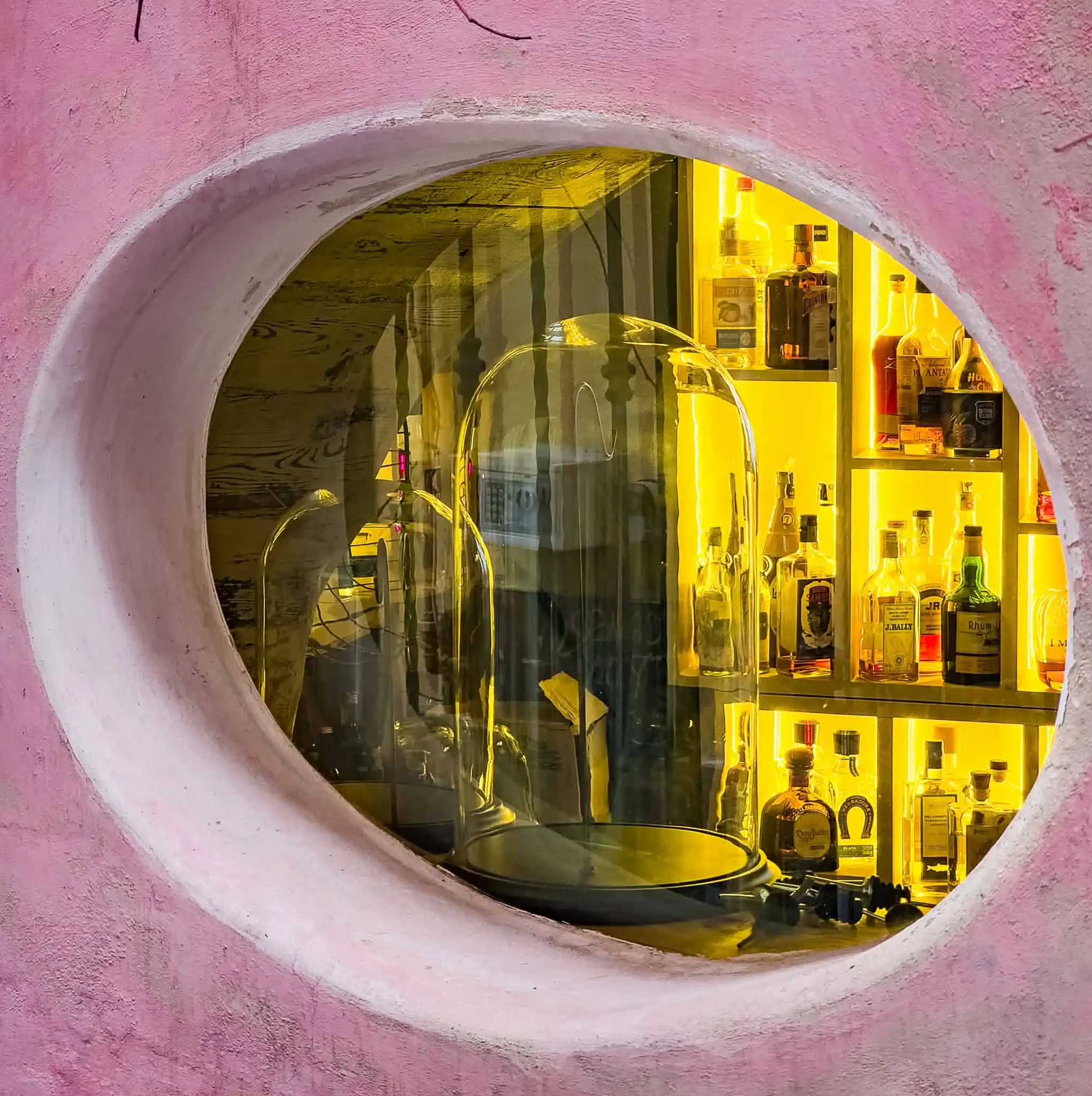 חלון עגול עם בקבוקי אלכוהול מוארים באור צהוב חם, מתאים לסדנת קוקטיילים