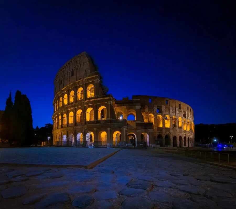 הקולוסיאום המרשים של רומא מואר באור חמים בשעת לילה שקטה, על רקע שמיים כחולים עמוקים